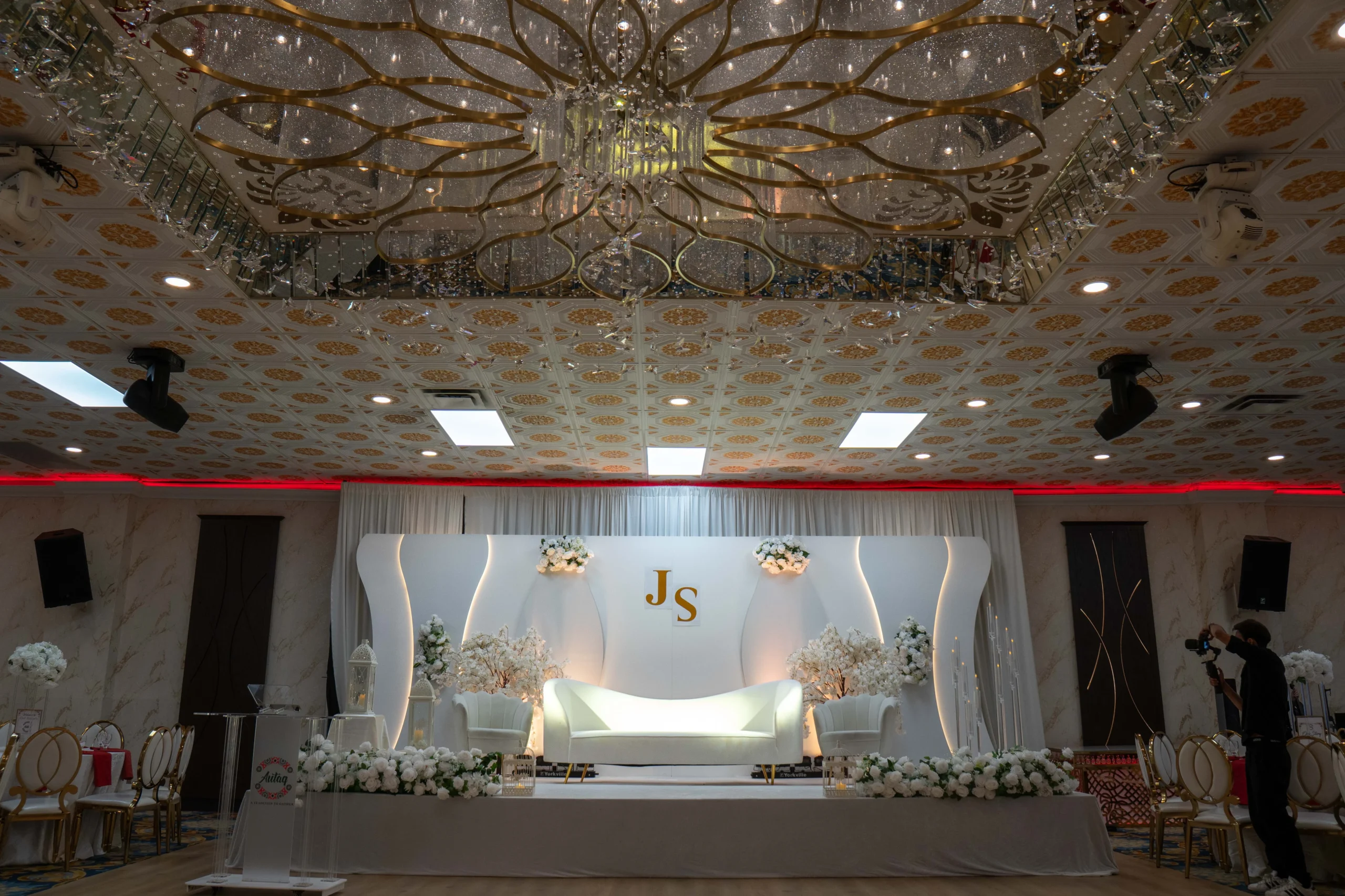 Elegant indoor wedding venue with decorated reception tables, floral centrepieces and gold chairs.
