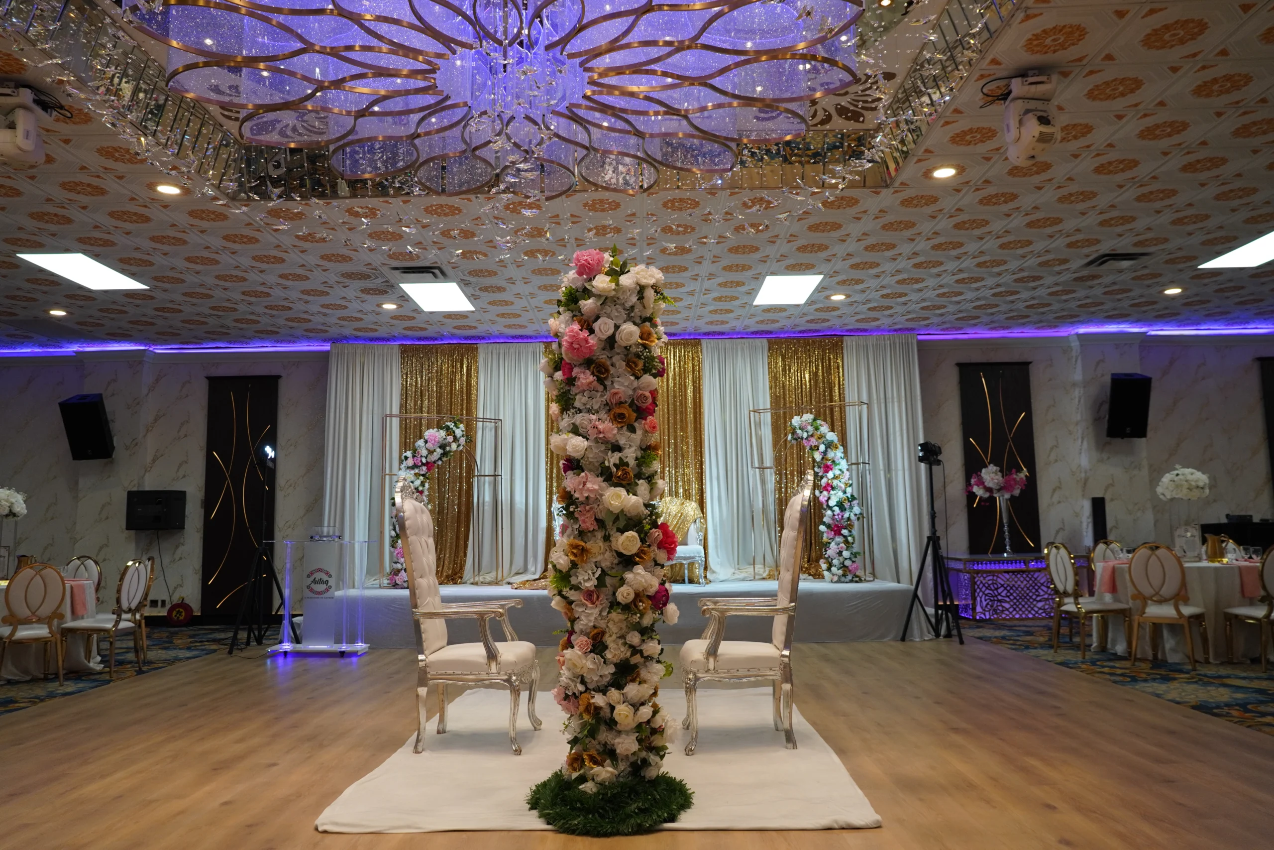 Muslim couple seated at an elegantly decorated Nikah ceremony in a banquet hall with floral arrangements and family guests.